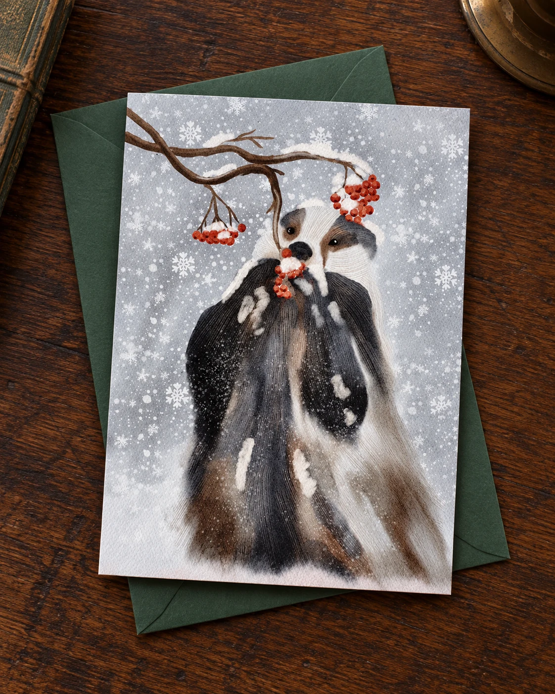 Winter Badger borderless 5 × 7 inch greeting card on a green envelope on an oak desk